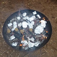 Die Kartoffelpakete landen in der Glut! Ein paar Kartoffeln bekommen einen Lehmmantel.